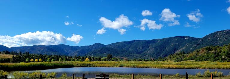 Image of front range with pond in front and blue sky with puffy clouds